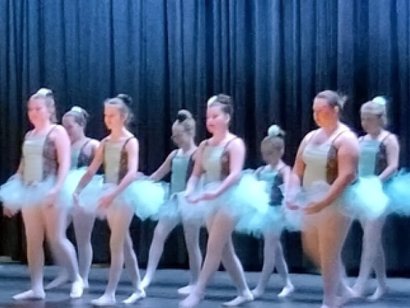 A group of McDowell Choices kids are performing ballet on a stage with a blue curtain backdrop.