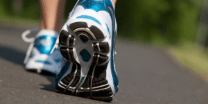 Close-up of the sole of a blue and white running shoe mid-stride on a paved path with greenery blurred in the background