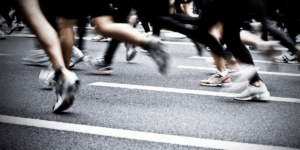 Blurred motion of runners&rsquo; legs and sneakers crossing a street during a race, with white lane markings visible on the pavement